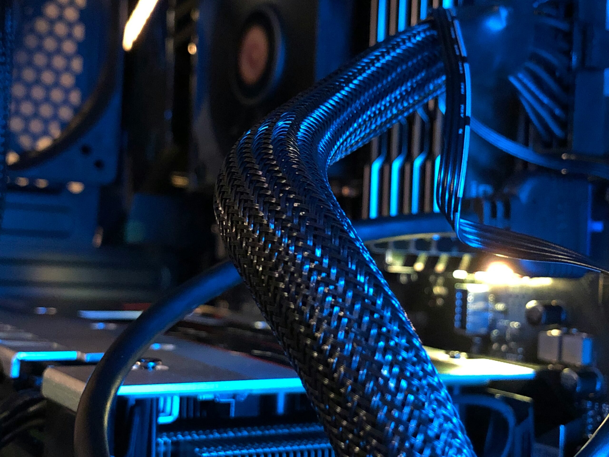 A close-up view of the interior of a computer, showing braided cables, cooling components, and circuit boards illuminated by blue light. Photo by Sean D on Unsplash