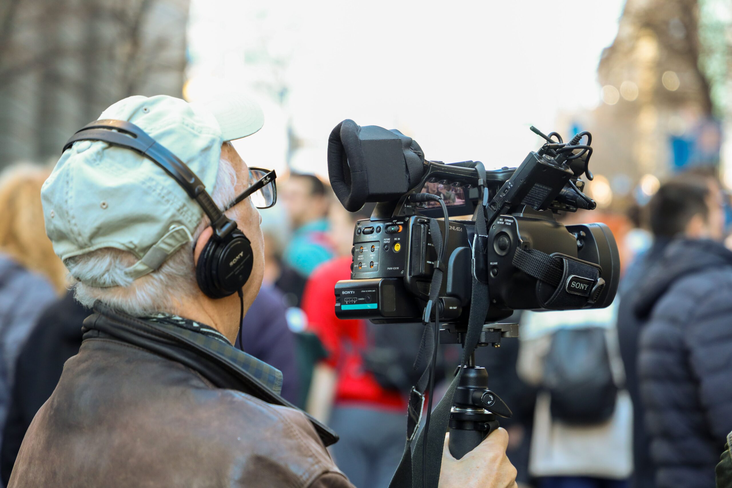 A man wearing headphones is behind a camera, filming a crowd of people. Photo by Boris Hamer in Pexels.